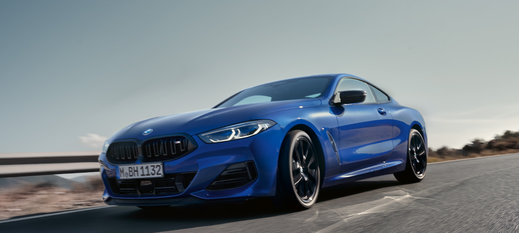 BMW Serije 8 Coupé G15 LCI Facelift 2022 BMW M850i xDrive M Portimao plave metalik boje prednji prikaz vozila iz niskog ugla tokom vožnje po seoskom putu sa brdima u pozadini